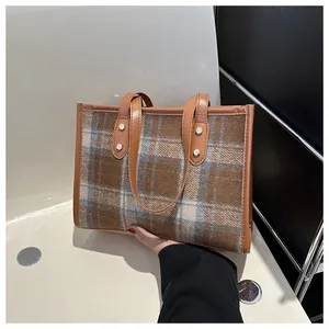 Detail of checkered fabric handbag with brown leather handles and gold rivet accents