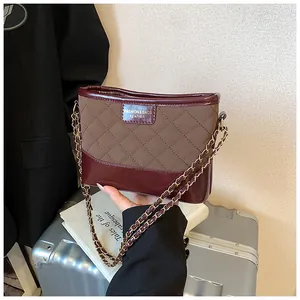 Détail de la couture en treillis marron et du cuir verni bordeaux du sac à bandoulière