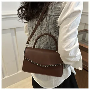 Detail of dark brown leather crossbody bag with silver rivets and golden hardware