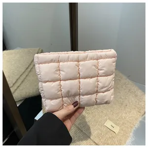 Handheld view of a peach-colored quilted puffer clutch with classic square stitching detail