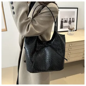 Détail d'un sac cabas tressé noir avec un nœud papillon porté à l'épaule par un mannequin