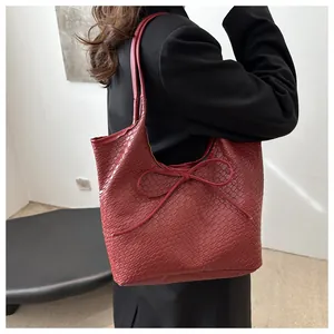 Détail du cabas tressé rouge foncé avec un nœud décoratif sur une surface en similicuir