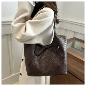Détail du sac cabas en cuir tressé marron foncé avec nceud décoratif porté à l'épaule