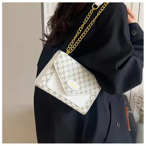Détail du sac à bandoulière blanc avec motifs marrons et une grosse chaîne dorée