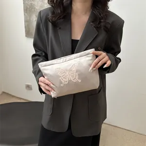 Borsa da trucco in raso beige con ricamo a farfalla tenuta da una modella elegante