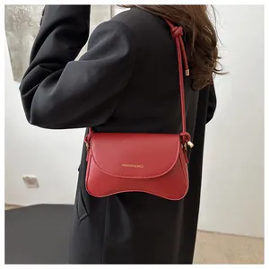 Close-up of red crossbody bag with wave bottom design and gold lettering on black blazer