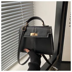 Detalle de bolso negro con costuras blancas en contraste y cierre dorado giratorio