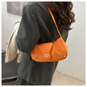 Close-up of bright orange crescent bag with gold rotary lock and rivet strap details