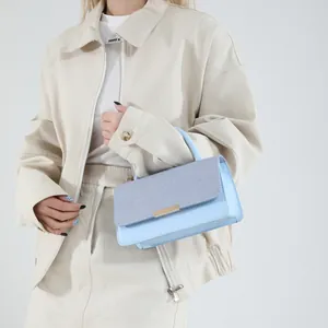 Sac à main bleu clair en cuir avec rabat texturé et barre dorée porté par un mannequin