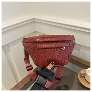 Detail of burgundy woven texture on waist bag with adjustable strap and front zipper pocket