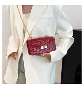 Detail of burgundy crocodile pattern crossbody bag with gold chain on white blazer