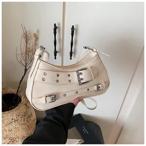 Close-up of beige moon-shaped shoulder bag with silver eyelet straps and buckles