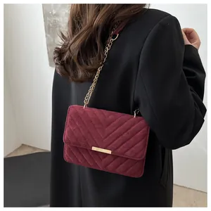 Detail of burgundy suede shoulder bag with V-shaped quilting and gold chain strap
