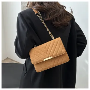 Close-up of tan suede chevron crossbody bag with gold chain strap on a black blazer