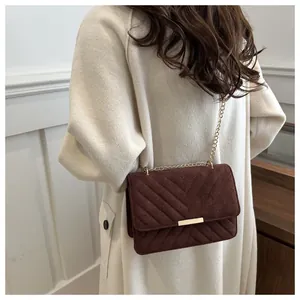 Detail of burgundy quilted suede crossbody bag with elegant gold chain on shoulder