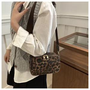 Detailed view of leopard print crossbody bag with double zippers and brown strap