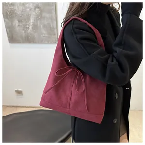 Detail of burgundy suede shoulder bag featuring a decorative bow tie and matte texture