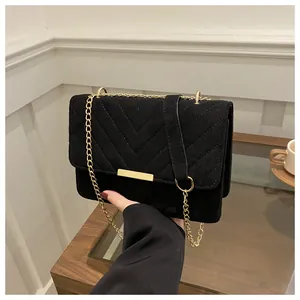 Detail of black suede shoulder bag with V-shaped quilting and gold metal chain strap