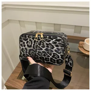 Detail of leopard print crossbody bag with dual gold zippers and wide nylon strap