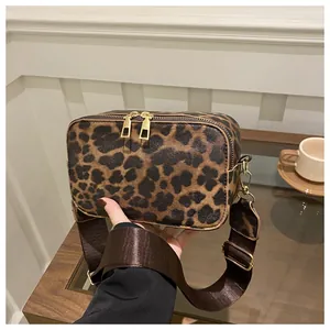 Detail of leopard print crossbody bag with gold zippers and brown nylon strap