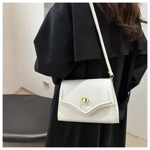 Detail of the golden oval turn-lock closure on a white minimalist shoulder bag
