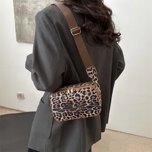 Leopard print crossbody bag with wide brown strap shown on a gray blazer model