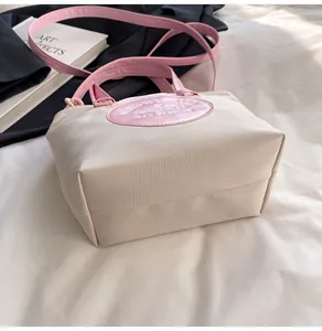 Détail du sac seau en nylon contrasté avec patch brodé rose et poignée sur un lit