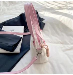 Détail du sac seau en nylon contrasté avec anses roses et breloque tissée sur tissu blanc