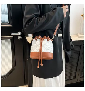 Detail of quilted drawstring bucket bag featuring white fabric and brown leather trim