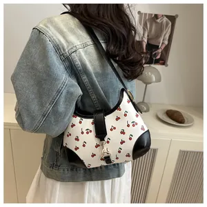 Detail of white tote bag with red cherry print featuring black leather trim and gold hook