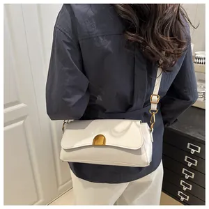 Détail d'un sac à bandoulière en cuir blanc avec une boucle magnétique dorée semi-circulaire