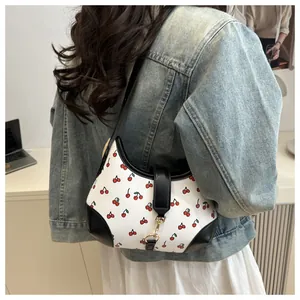 Close-up of white shoulder bag with cherry print and black leather trim and metal clasp