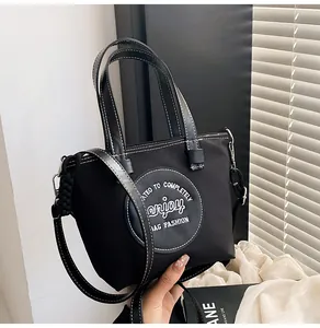 Détail du sac seau en nylon noir avec surpiqûres blanches et écusson logo circulaire