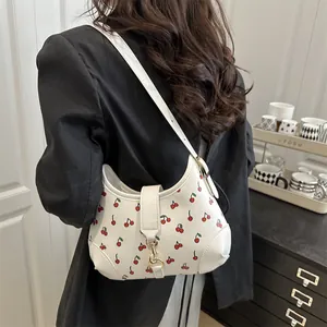 Chic white shoulder bag with red cherry prints and golden hardware worn by a model