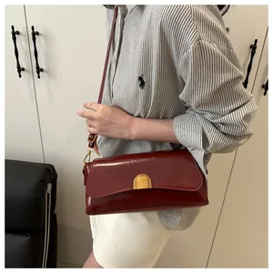 Détail du sac bandoulière en cuir bordeaux avec boucle dorée sur chemise à rayures