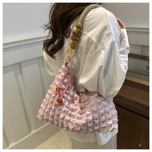 Détail du sac bandoulière rose gaufré avec texture plissée et lanière en perles de bois