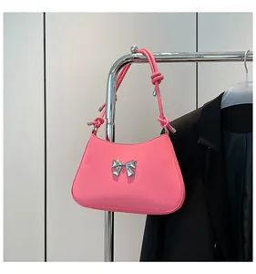 Détail d'un sac sous le bras rose avec nœud métallique argenté et bandoulière à nœuds