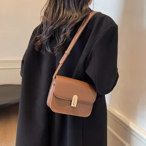 Petit sac bandoulière marron en cuir avec fermoir doré porté sur un manteau noir