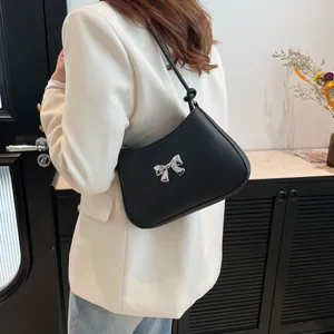 Sac sous le bras en cuir noir avec nœud argenté, porté avec un blazer blanc élégant