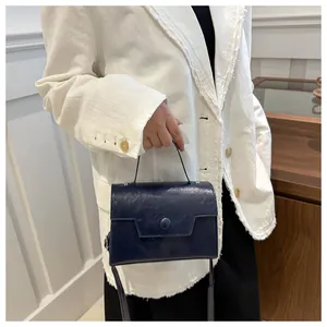 Détail du sac bandoulière bleu marine avec poignée porté sur une veste de tailleur blanche