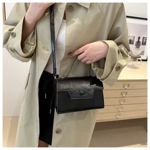 Détail d'un sac à main rectangulaire noir brillant avec rabat géométrique et poignée