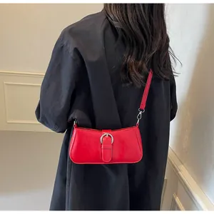 Detail of red minimalist shoulder bag with silver buckle worn by model against a black outfit