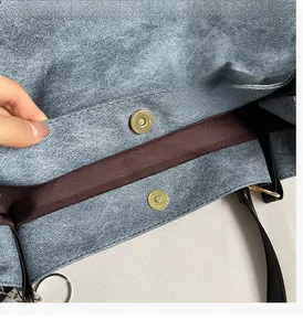 Detail of blue denim tote bag with shiny gold magnetic clasps and brown interior lining