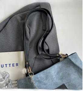 Detail of grey-blue tote bag with black leather handles and silver chain on a blazer