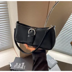 Detail of black faux leather baguette bag with silver buckle and smooth textured surface