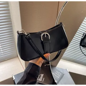 Detail of a minimalist black shiny faux leather shoulder bag with silver buckle accent