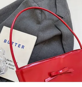 Detail of red patent leather bucket bag featuring a decorative bow and long shoulder strap