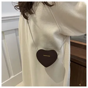 Détail d'un sac à bandoulière en forme de cœur marron foncé avec chaîne sur modèle