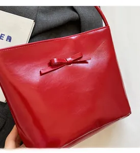 Detail view of red glossy bucket bag featuring a decorative bow and trapezoidal shape