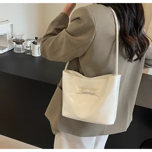 Close-up of a white leather bucket bag with a bow knot detail worn on shoulder